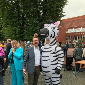 Kinderrechtefest Kommando Kids Zeven 2.6.2024; im Vordergrund v.l.n.r. stellv. Bürgermeisterin Martina Stelljes, Samtgemeindebürgermeister Henning Fricke und Maskotchen Zevi, im Hiuntergrund zu sehen sind das Rathaus und Gäste der Veranstaltung